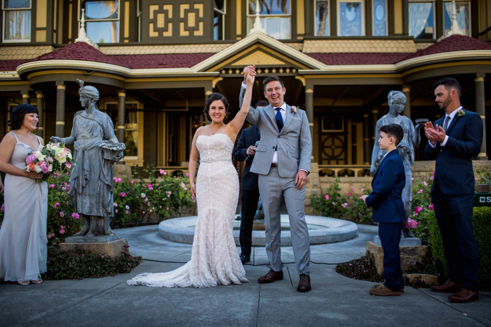 Bride and groom smiling and raising their hands after their wedding ceremony at the Winchester Mystery House in San Jose, CA