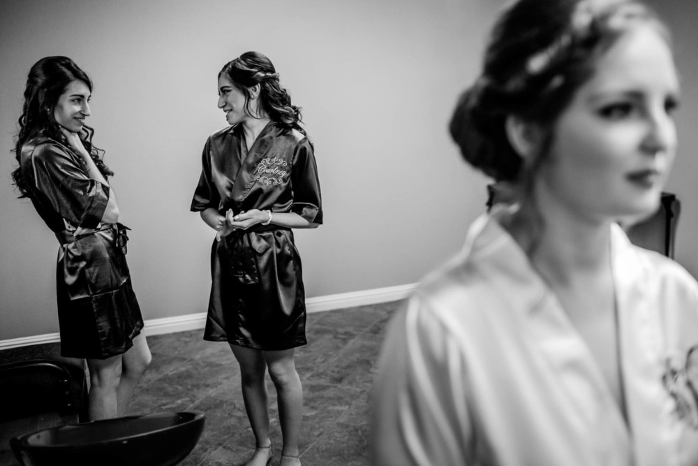 Two bridesmaids laughing as the bride has her makeup done