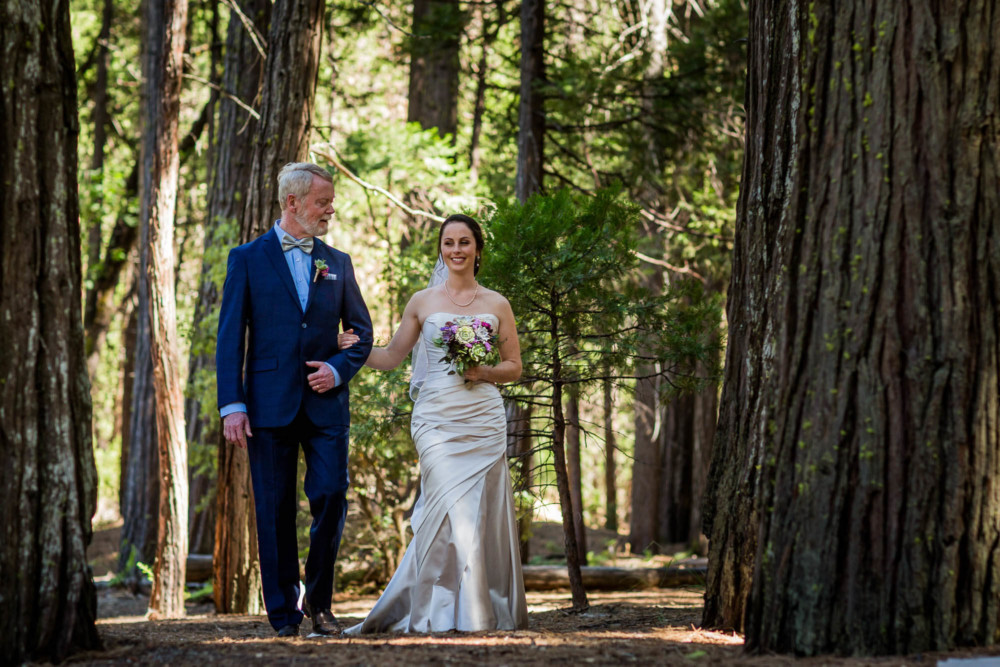 Father walks his daughter the bride down the aisle before the wedding on Cathedral Beach in Yosemite Valley