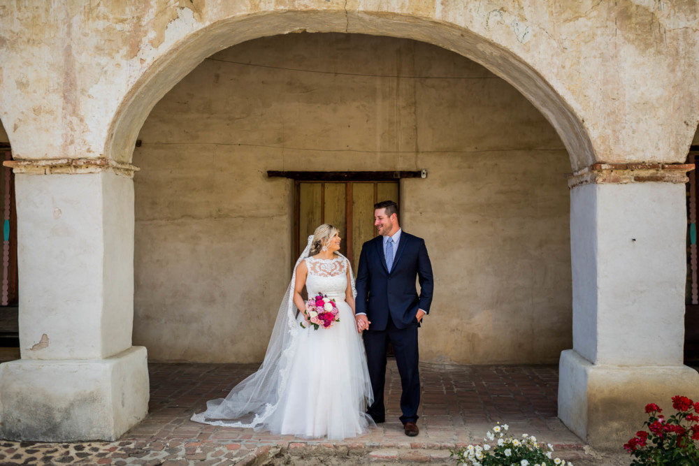 Portrait of the bride and groom under an arch at Mission San Miguel