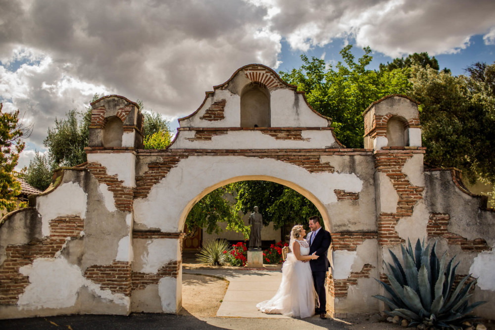 Portrait of the bride and groom under an arch at Mission San Miguel