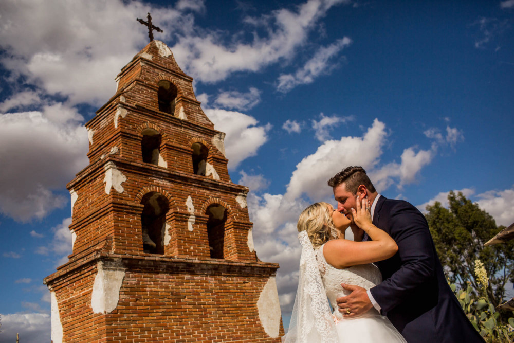 Portrait of a bride and groom in front of the bell tower at Mission San Miguel in Paso Robles, CA