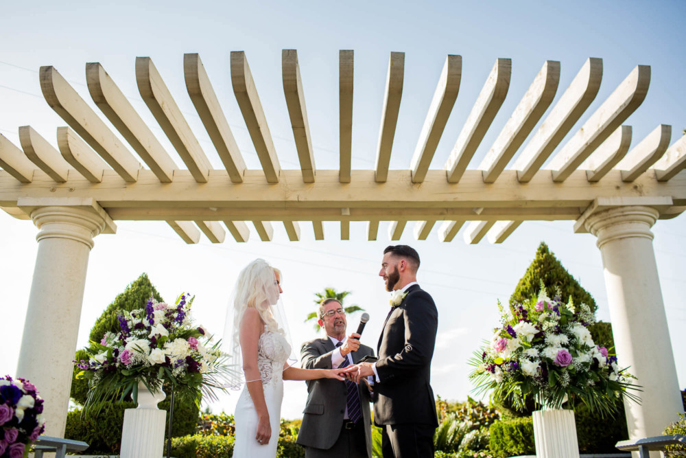 Groom places the ring on the bride's finger during their wedding at Copper River Country Club