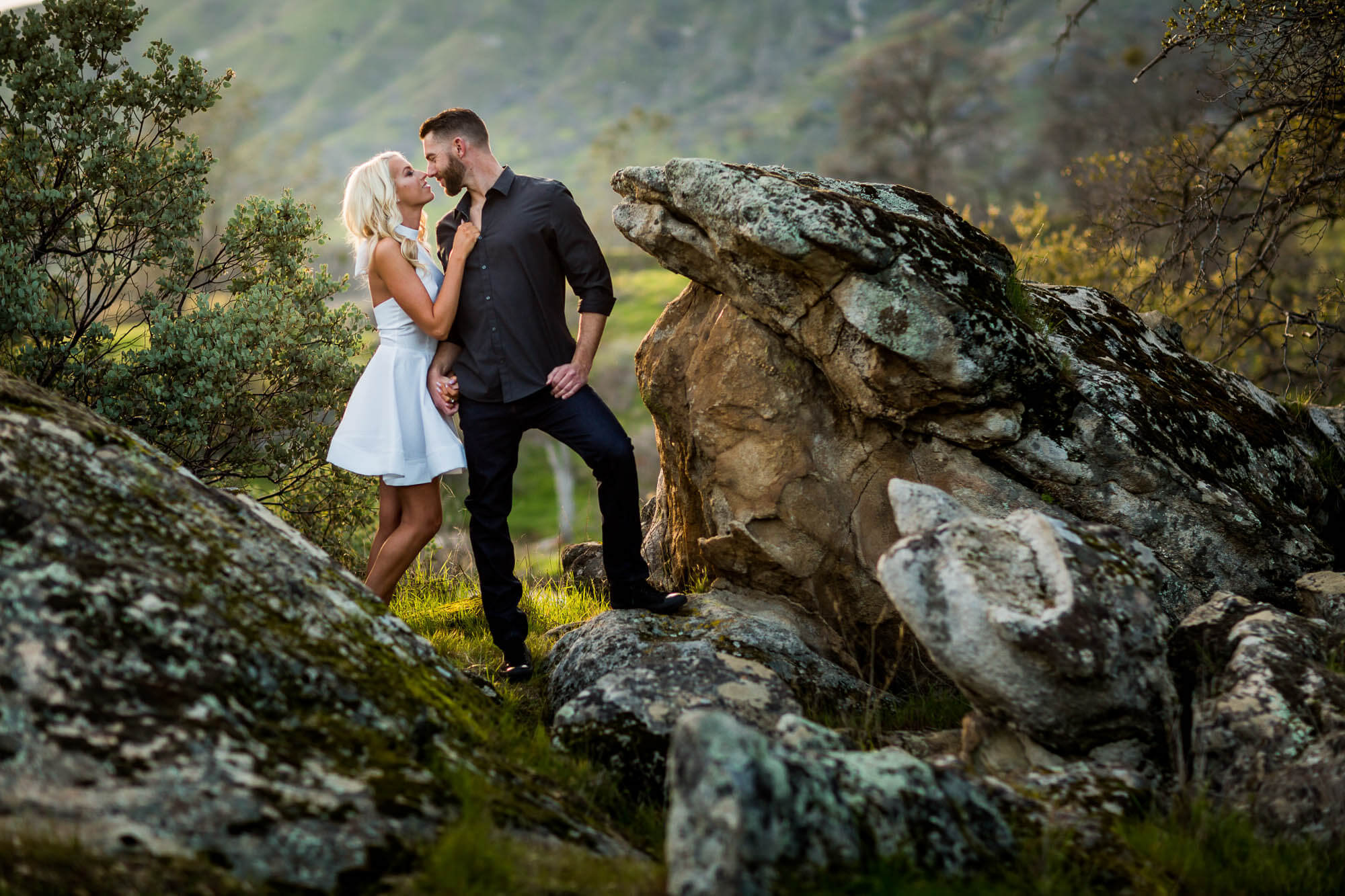 Portrait of a couple standing on a granite rock among green hills