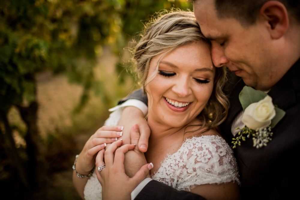 Snuggly portrait of the bride and groom in a vineyard at sunset.
