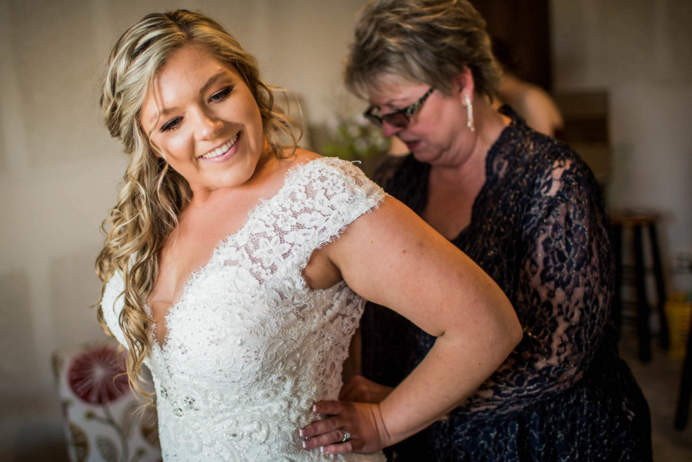 Mother of the bride helps the bride into her dress