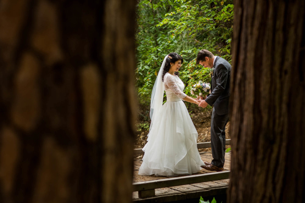Bride and groom laugh during their first look in the forest