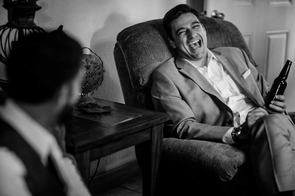 Friend laughs while holding a beer while the groom gets ready for his wedding