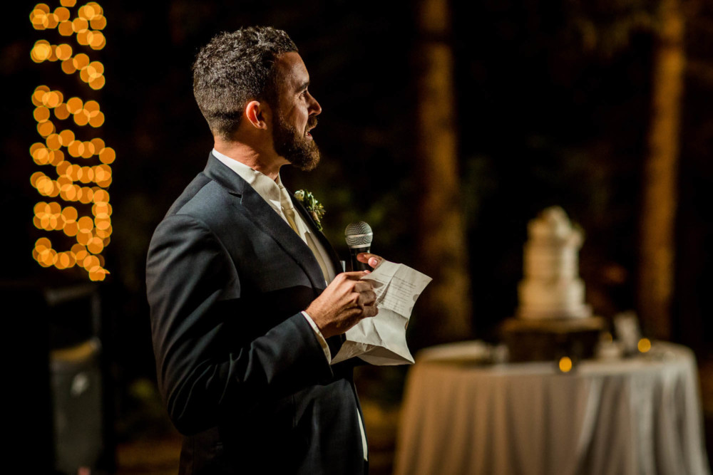 Best man gives a speech with the wedding cake in the background