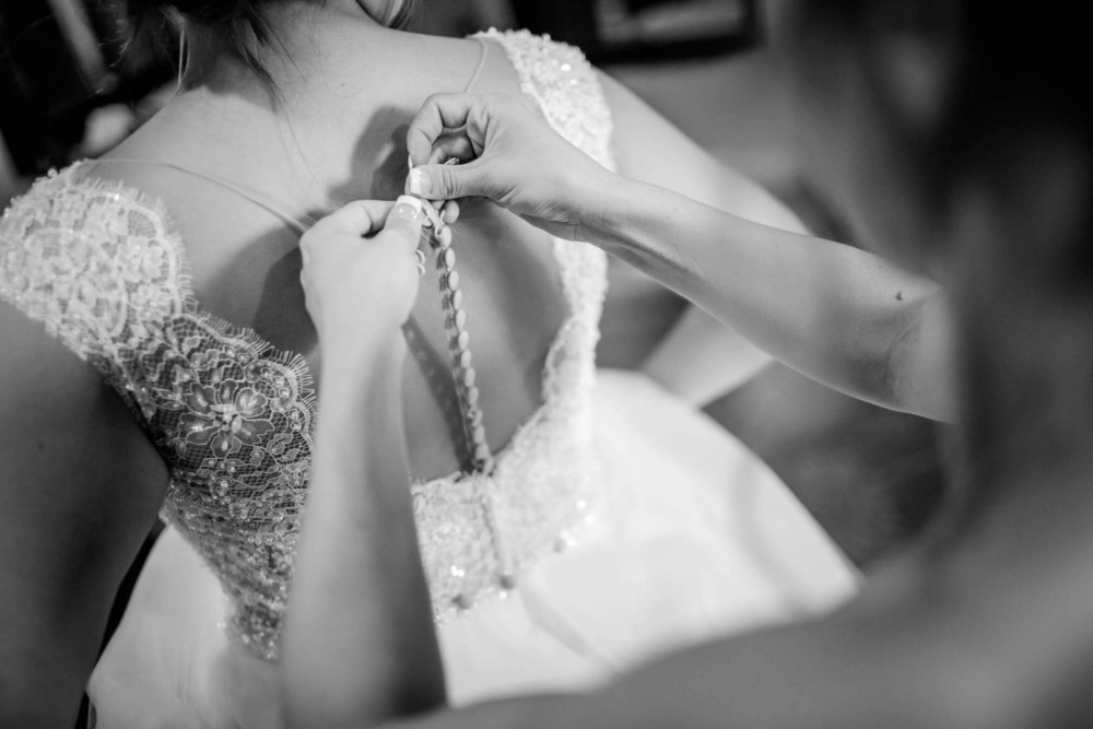 Bridesmaid buttoning bride's dress