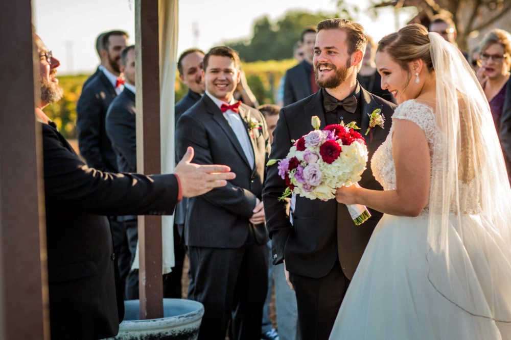 Bride and groom laugh with the officiant during their wedding ceremony