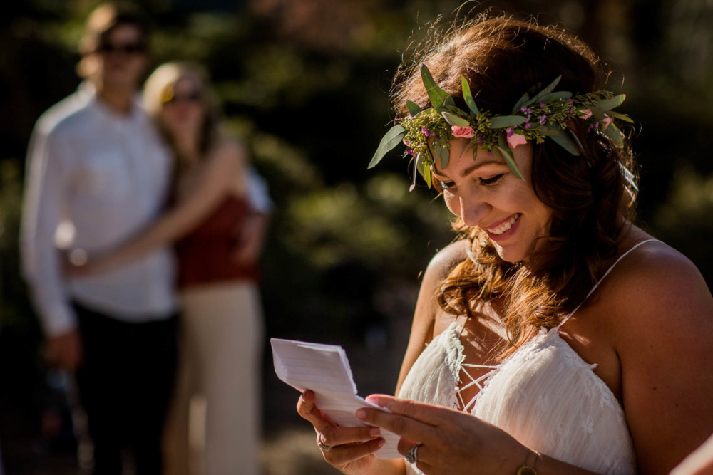 Bride laughs while reading her vows as a couple looks on during the wedding