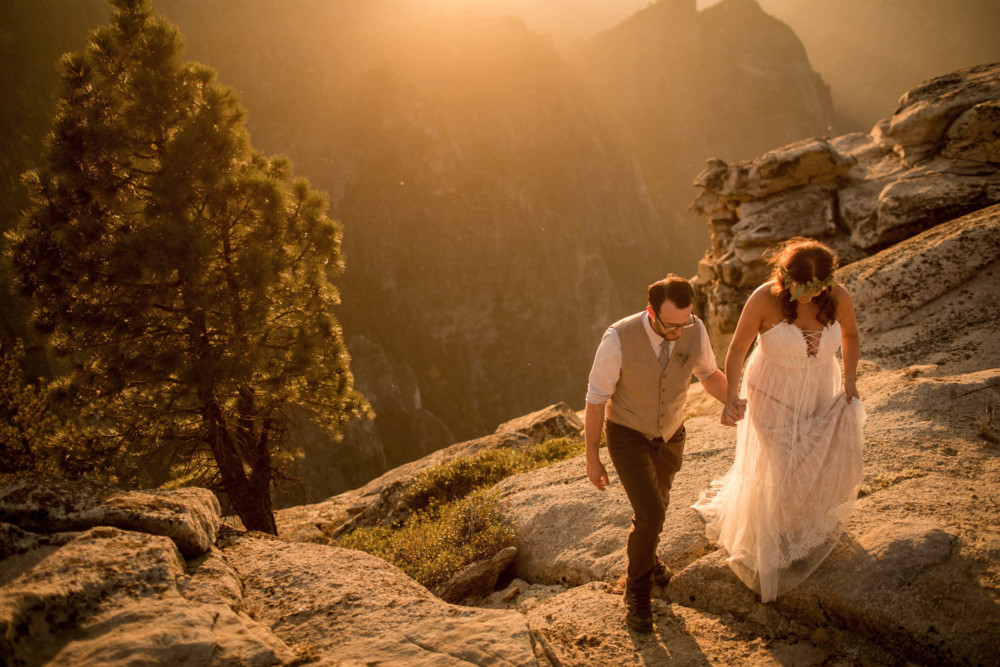Bride and groom walk up the rocks at Taft Point at sunset