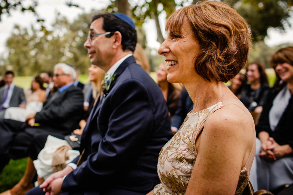 Mother and father of the groom react and smile during the wedding ceremony