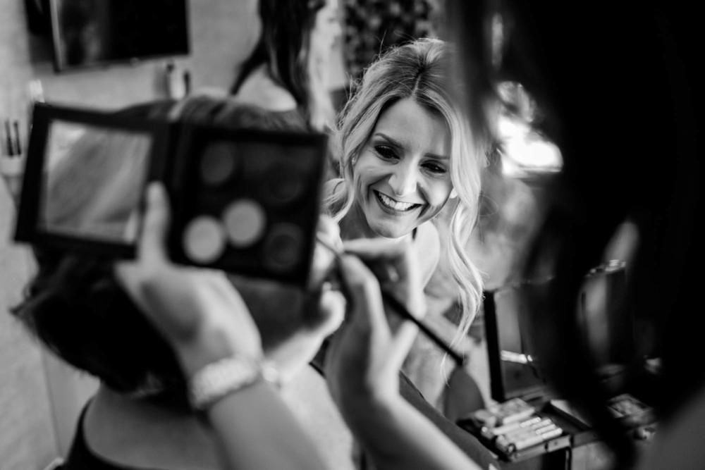bridesmaid laughs while looking at a friend getting her makeup done