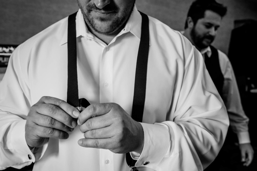 groom adjusting his suspenders while getting ready for the wedding