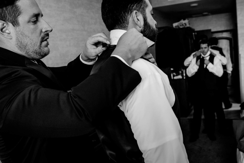 Groom adjusting the collar for a groomsmen