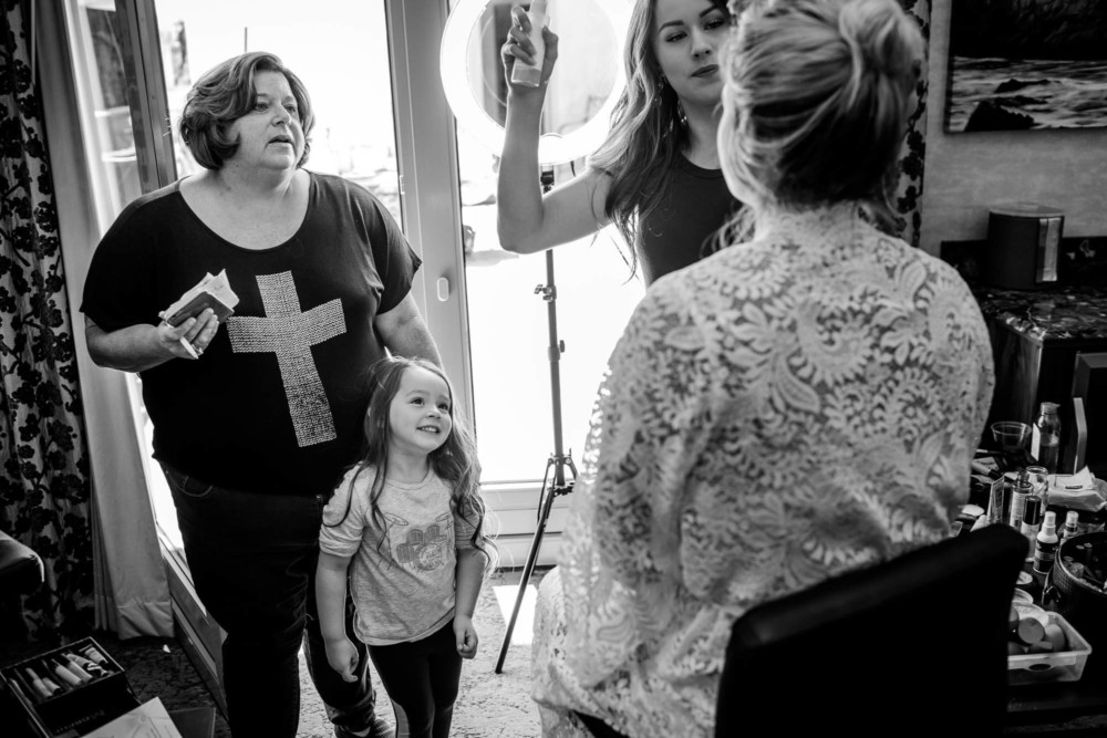 Friend of the bride and flower girl react to a bride sitting in the makeup chair