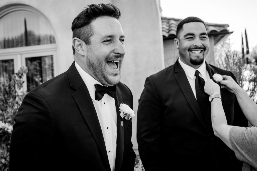 Groom laughs as a groomsmen has his boutonnière pinned