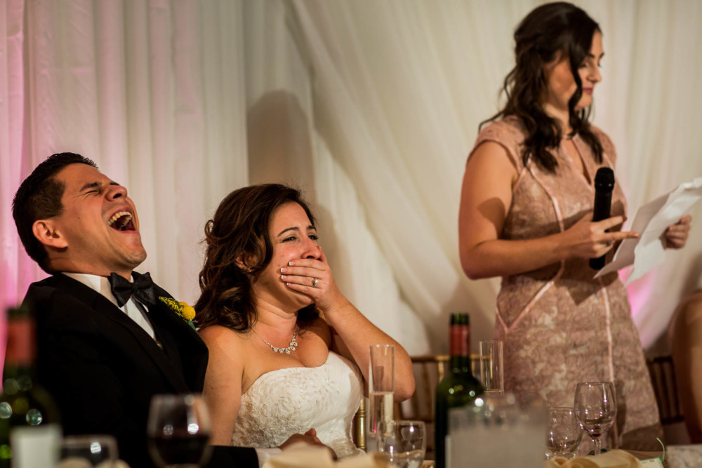 Bride and groom react with laughter during the wedding toasts