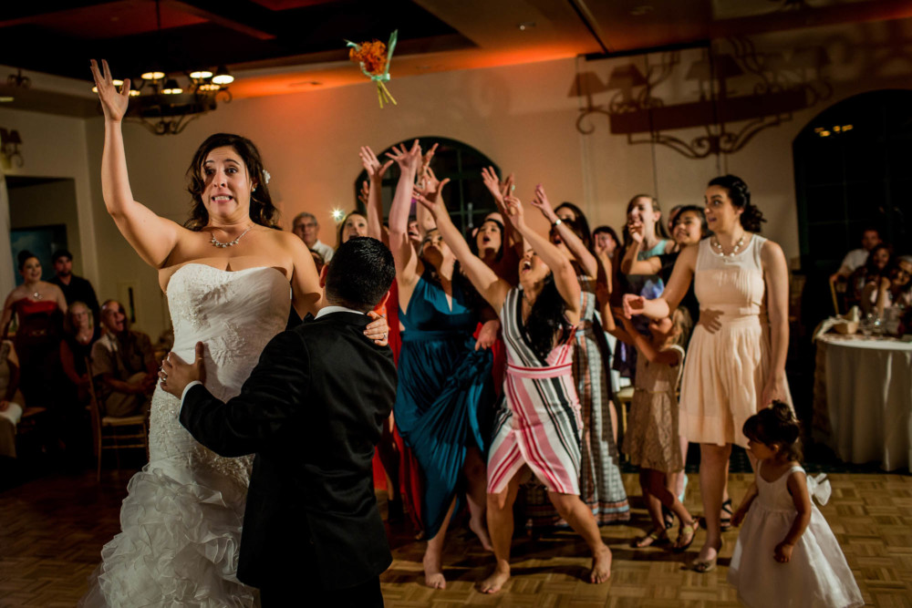 Bride throws bouquet while standing on chair at the wedding reception