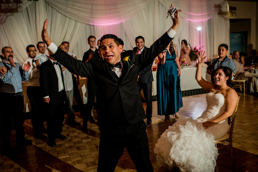Groom raises his arms in triumph after removing bride's garter