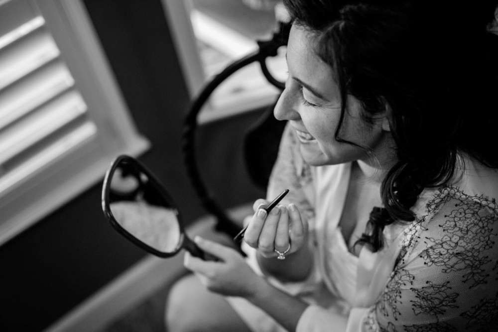 Bride checks her makeup in a mirror while getting ready for her wedding