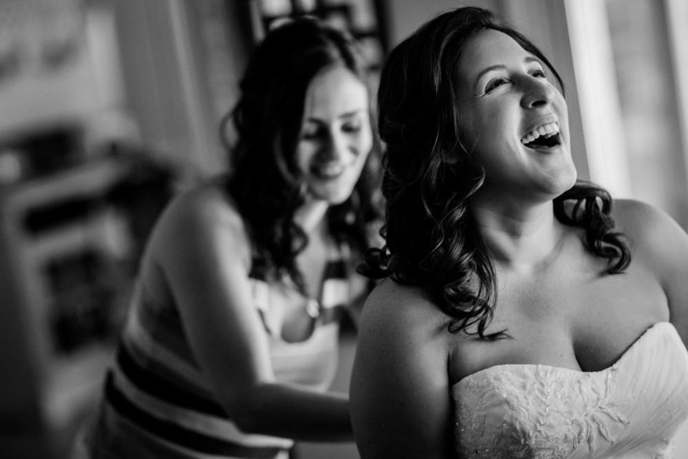 bride laughs while bridesmaid fastens her dress