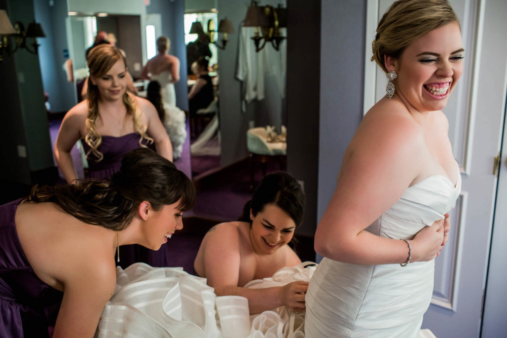 Bride laughs as bridesmaids struggle with her dress