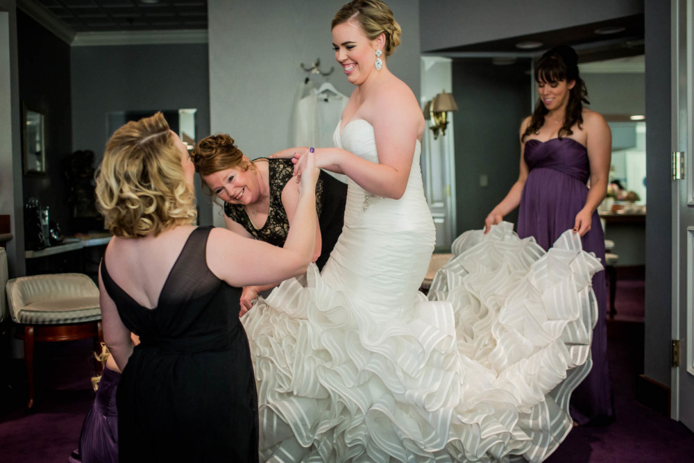 Mom holds bride's hand while bridesmaids fluff her dress