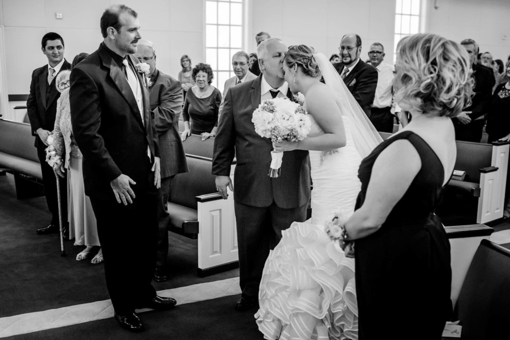 Father of the bride kisses his daughter while the groom and her mother watch