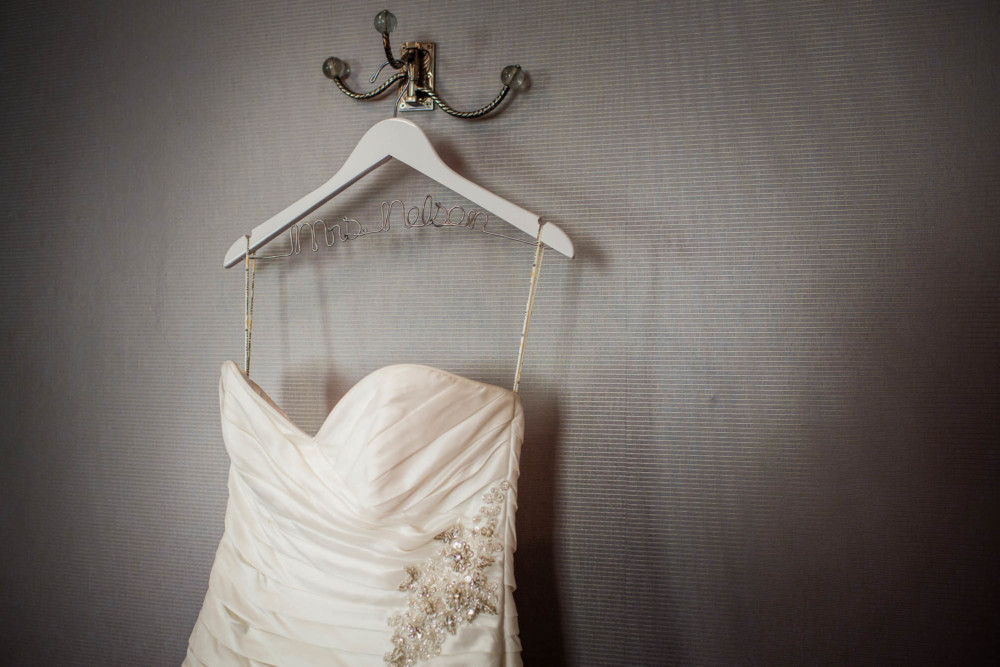 Detail of hanging bride's gown on a hanger customized with her name written in wire