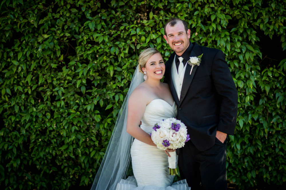 portrait of a bride and groom in front of a lush green hedge