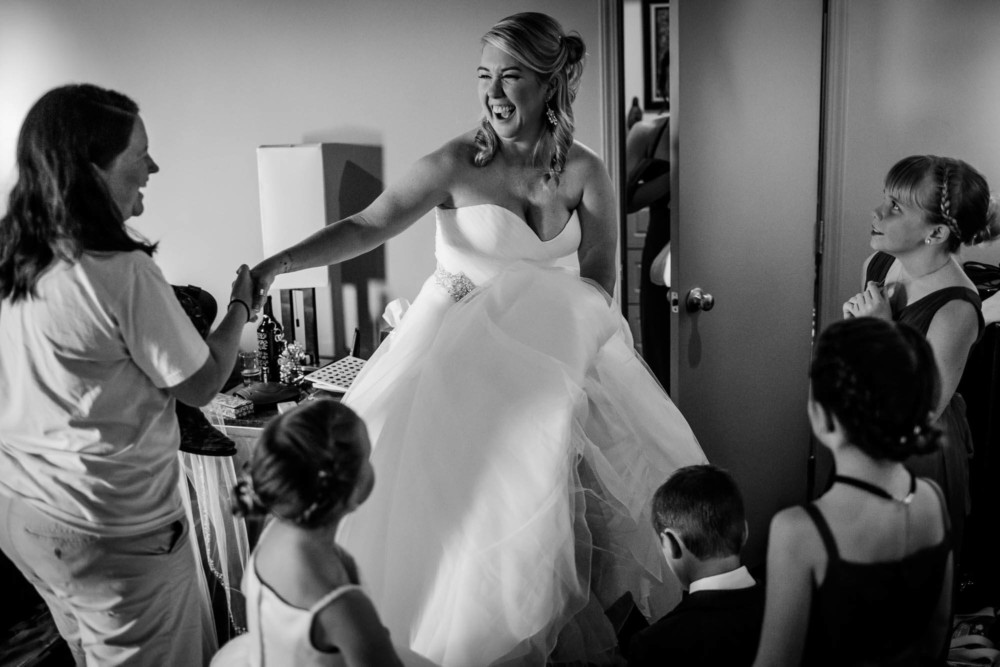Bride laughs as she's supported by a friend while putting on her boots