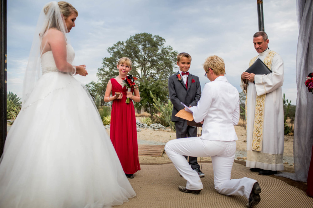Bride kneels while saying vows to her soon to be wife's son and daughter