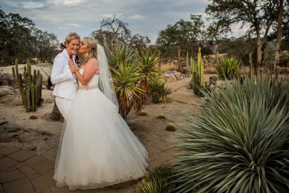 Bride kisses her wife on the cheek in a cactus garden