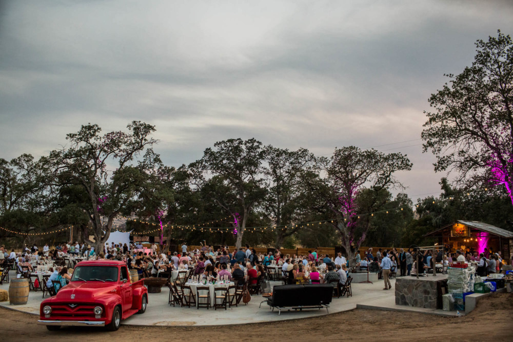 wide view of a wedding reception among large oaks with a vintage red pickup