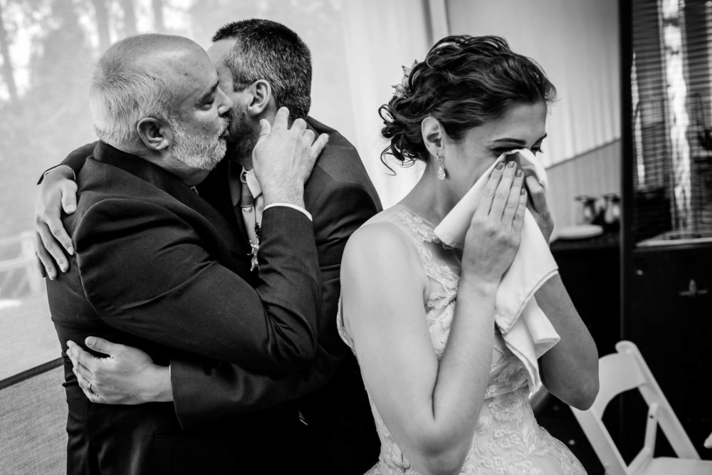 Bride wipes away tears after her fathers toast as he hugs her groom