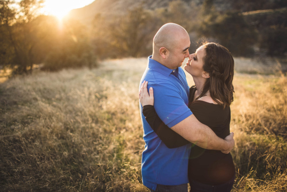 Couple gazes into each other's eyes as the setting sun flares behind them.