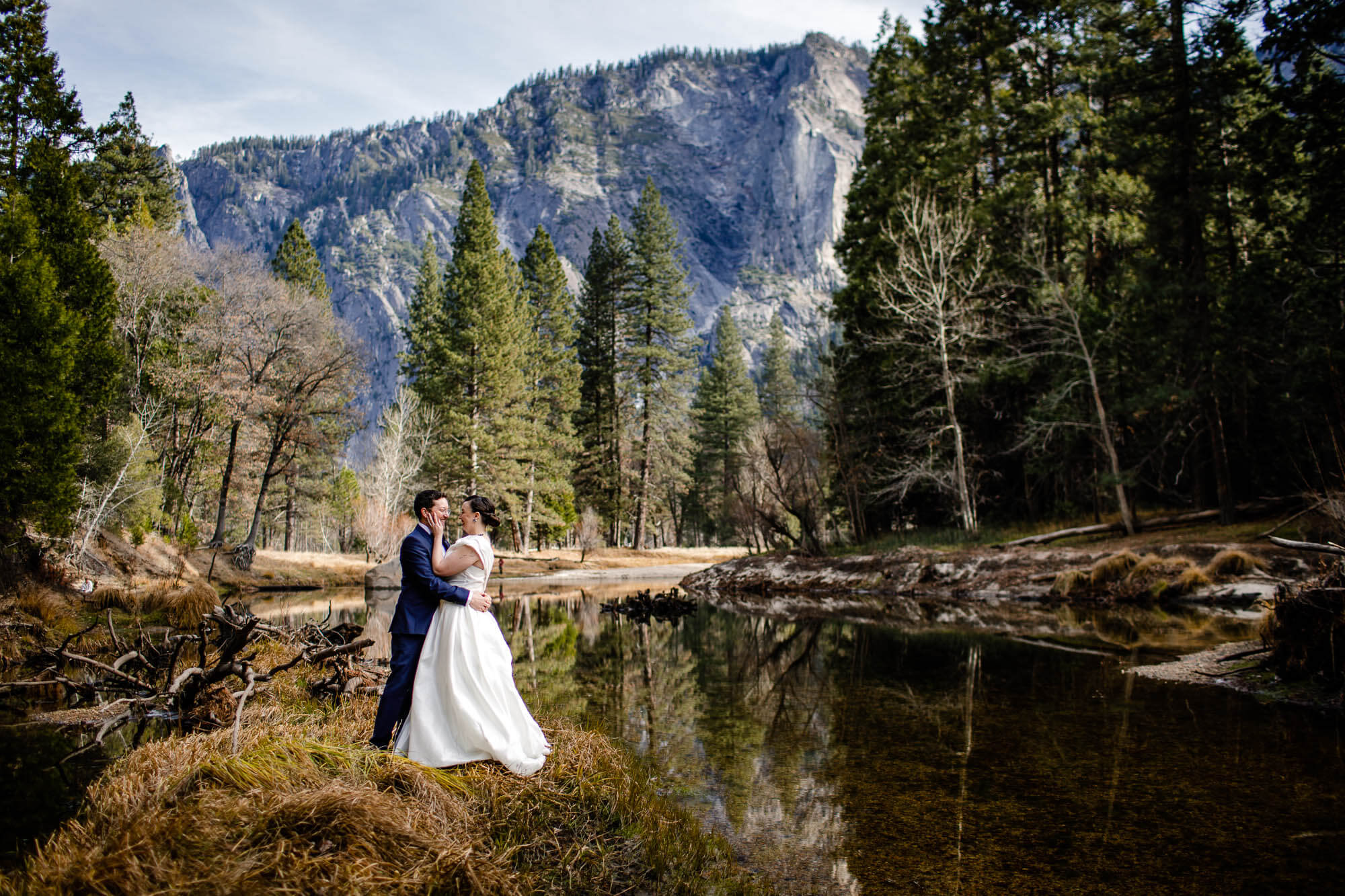Bride and groom kiss while standing on an island in the Merced River in Yosemite Valley
