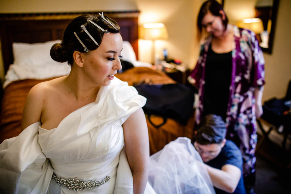 Bride glances back as her friends help her with her dress