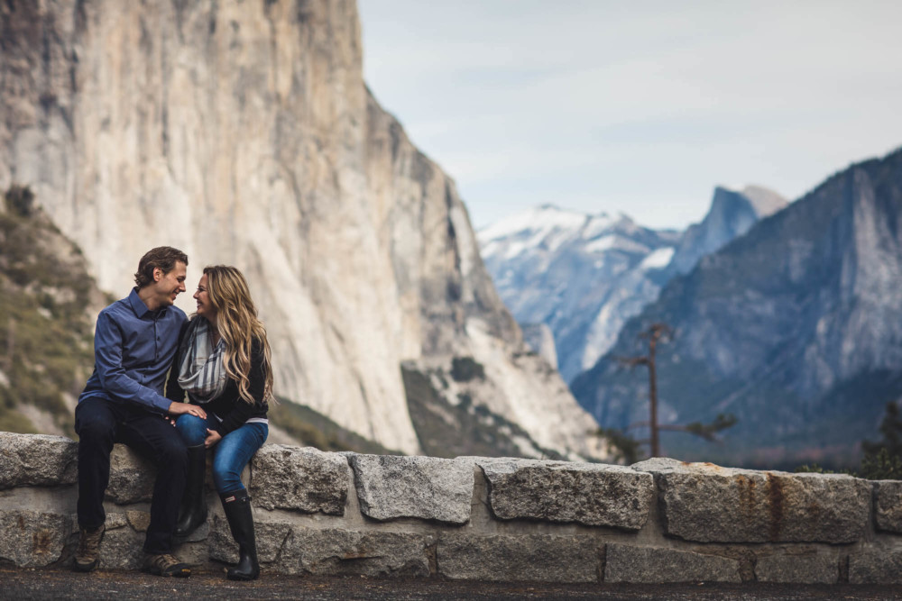 Couple sits on a wall in front of Yosemite Valley seen from Tunnel View