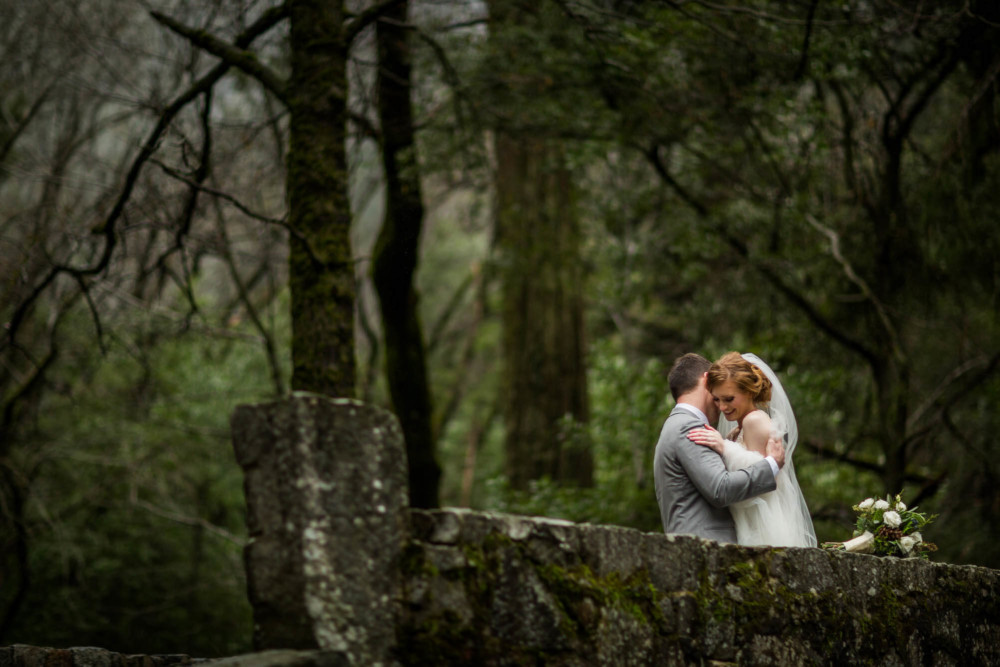 Bride and groom cuddle on a bridge below Bridalveil falls