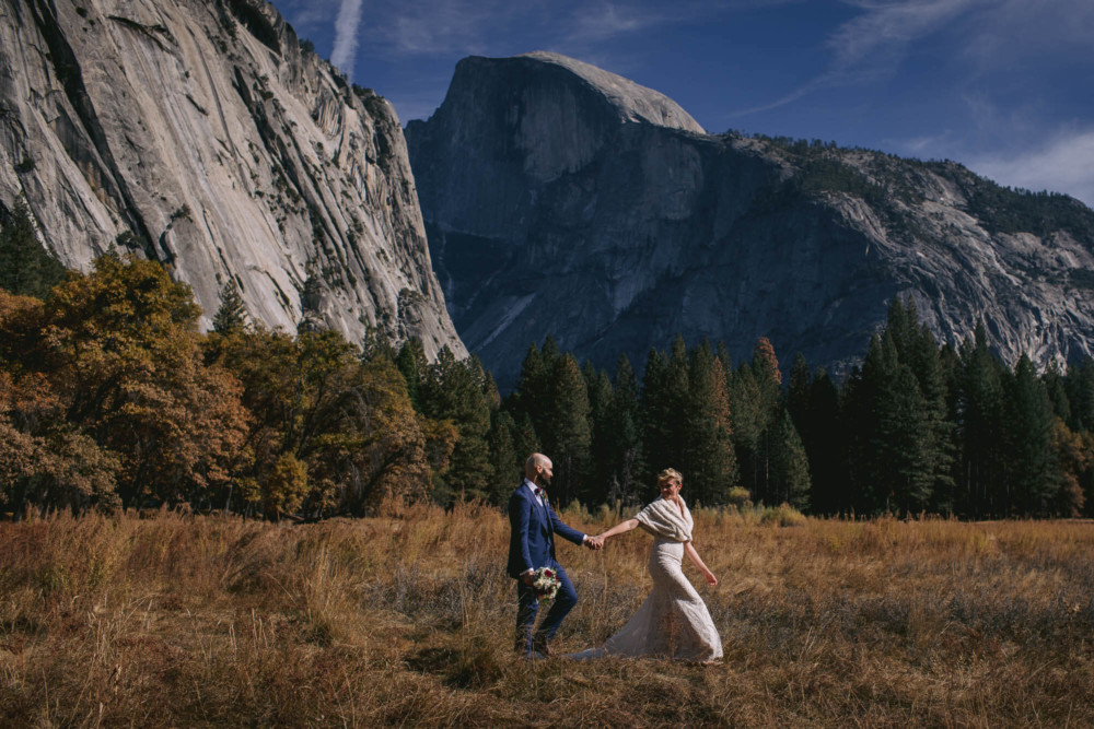 Bride and groom walk in Cooks Meadow below Half Dome in Yosemite National Park