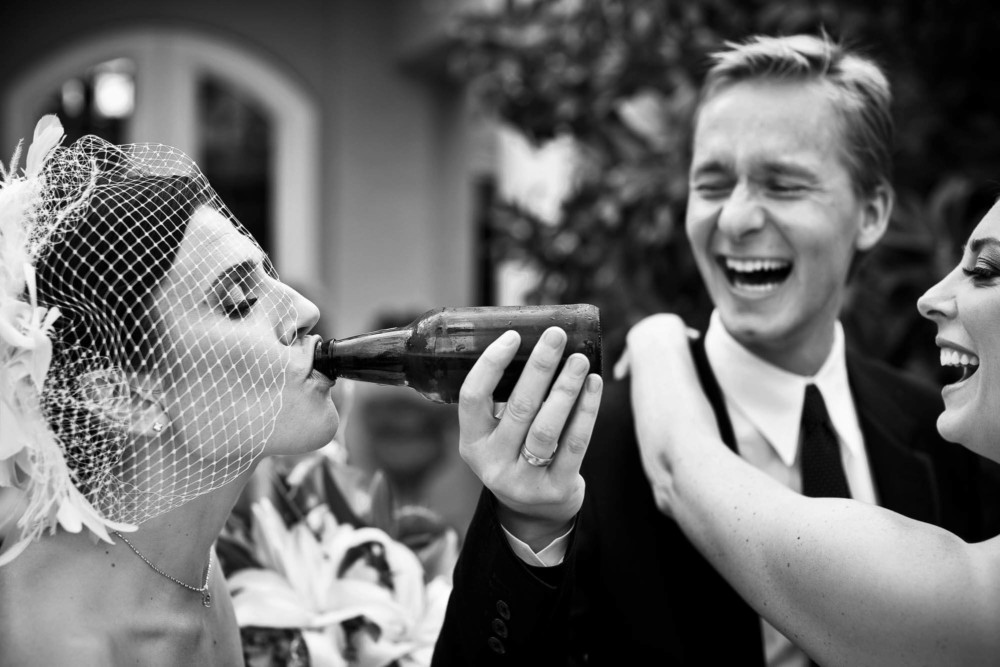 Friend feeds bride a beer while laughing
