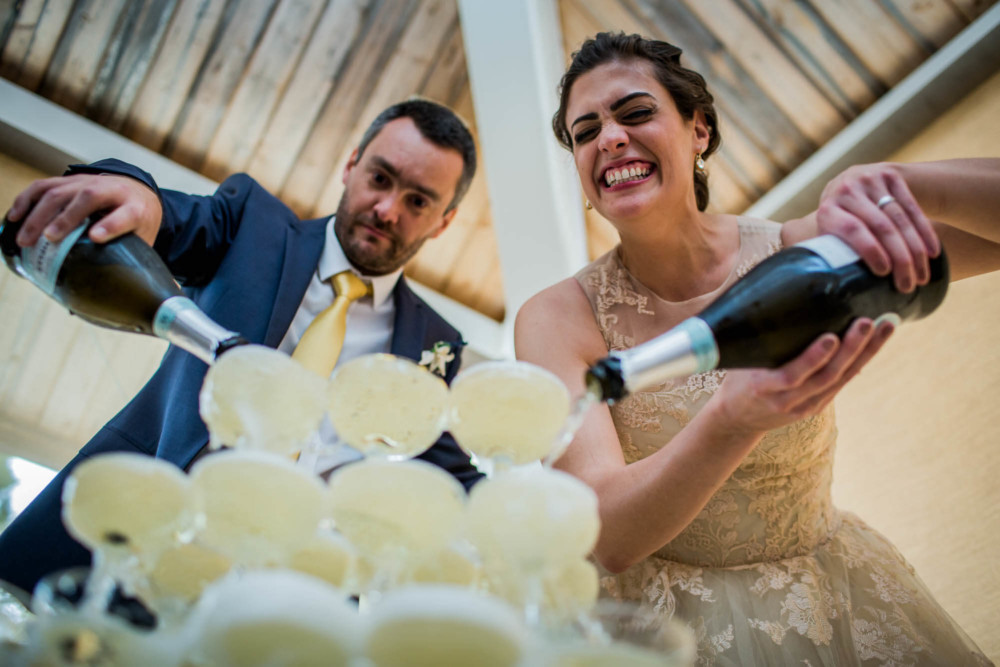 Bride and groom laugh as they pour champagne down a
