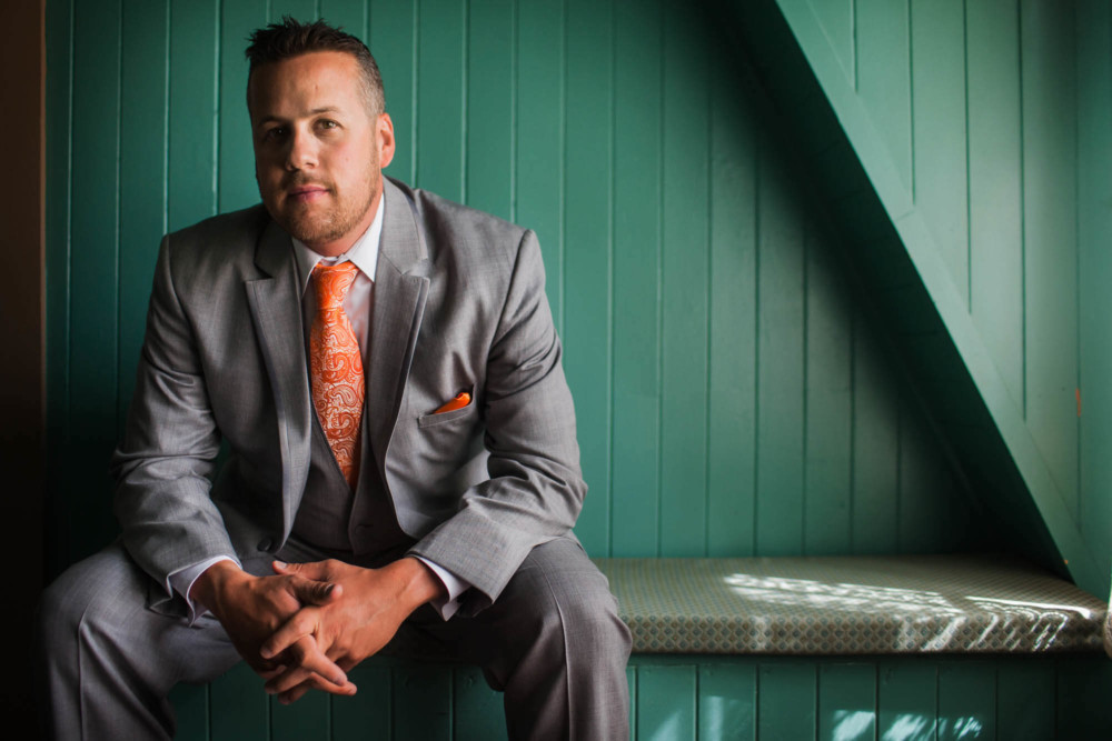 Portrait of a groom in a grey suit and orange tie against a green wall