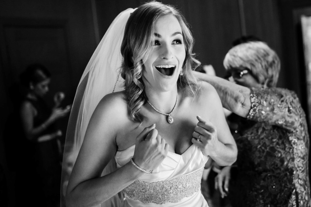 Bride holding her dress up as her mother fastens it
