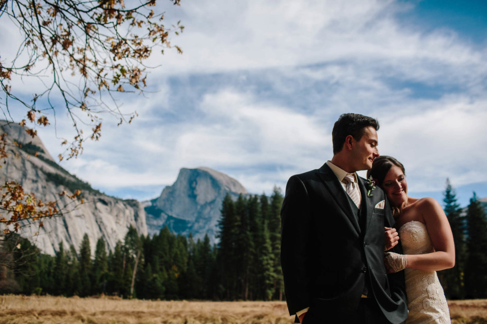 Bride and groom cuddling for a portrait in front of Half Dome in Yosemite National Park