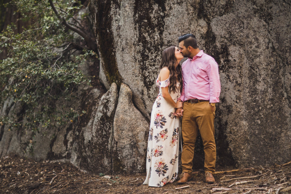 A couple kisses in front of a giant granite boulder